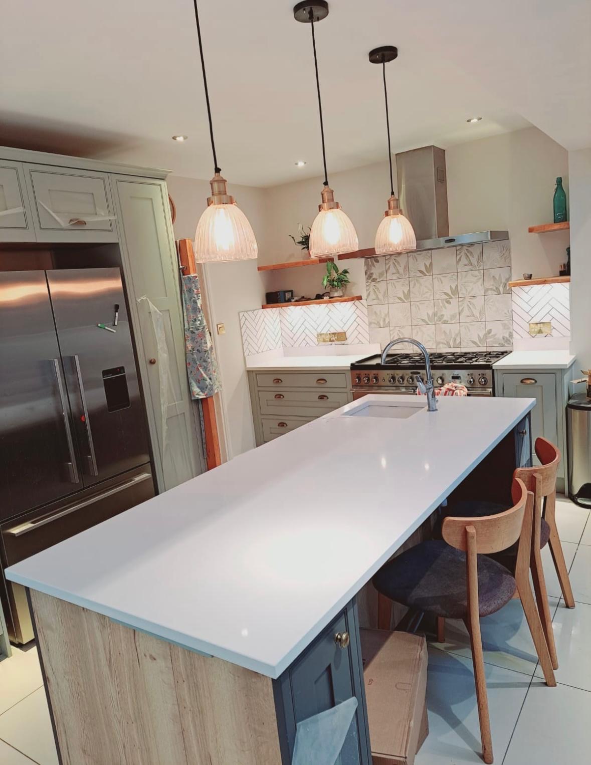Fitted kitchen with a central island, painted cabinetry and three pendant lights.