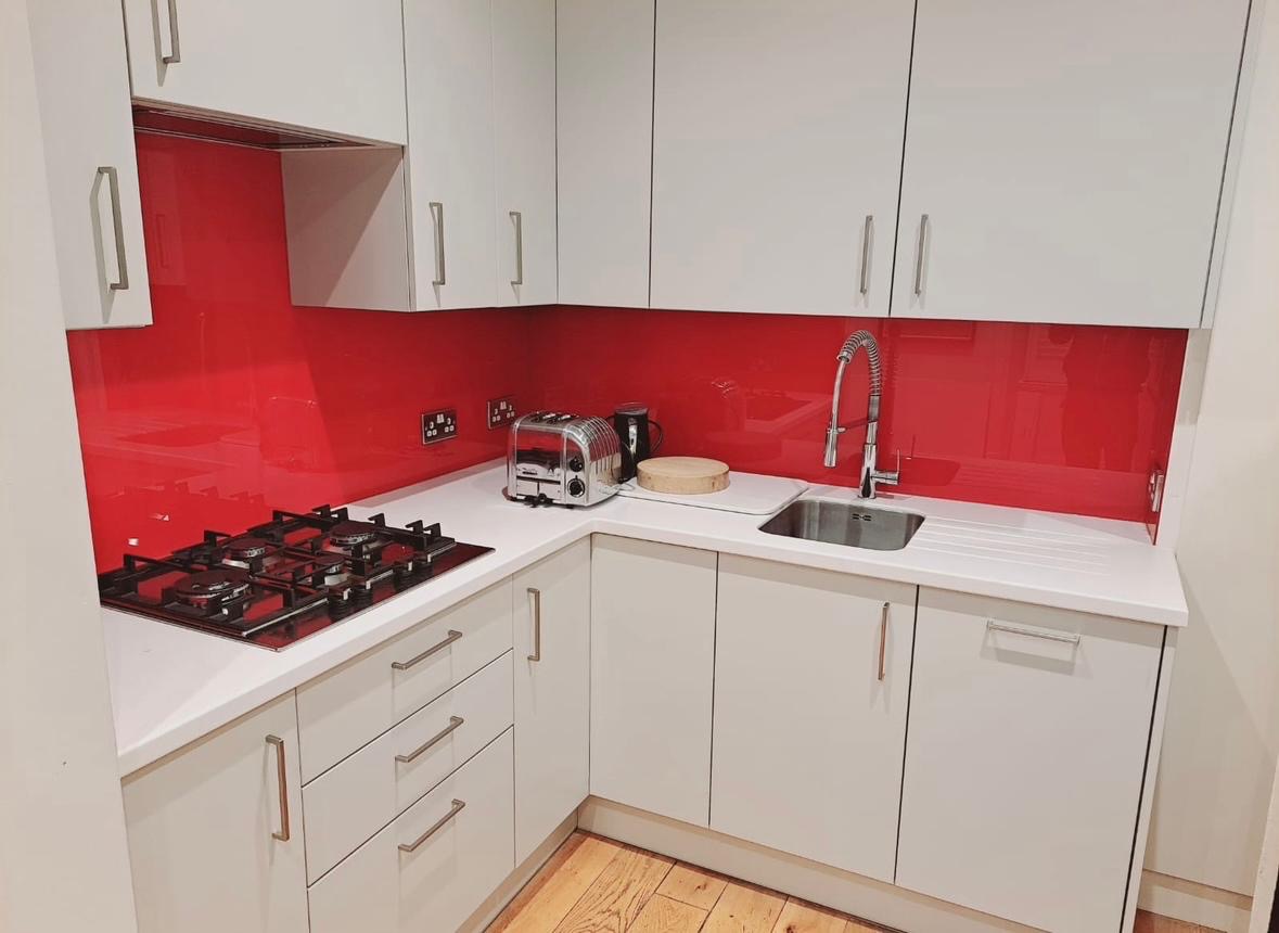 White kitchen cabinets with a red glass splashback and a gas hob.