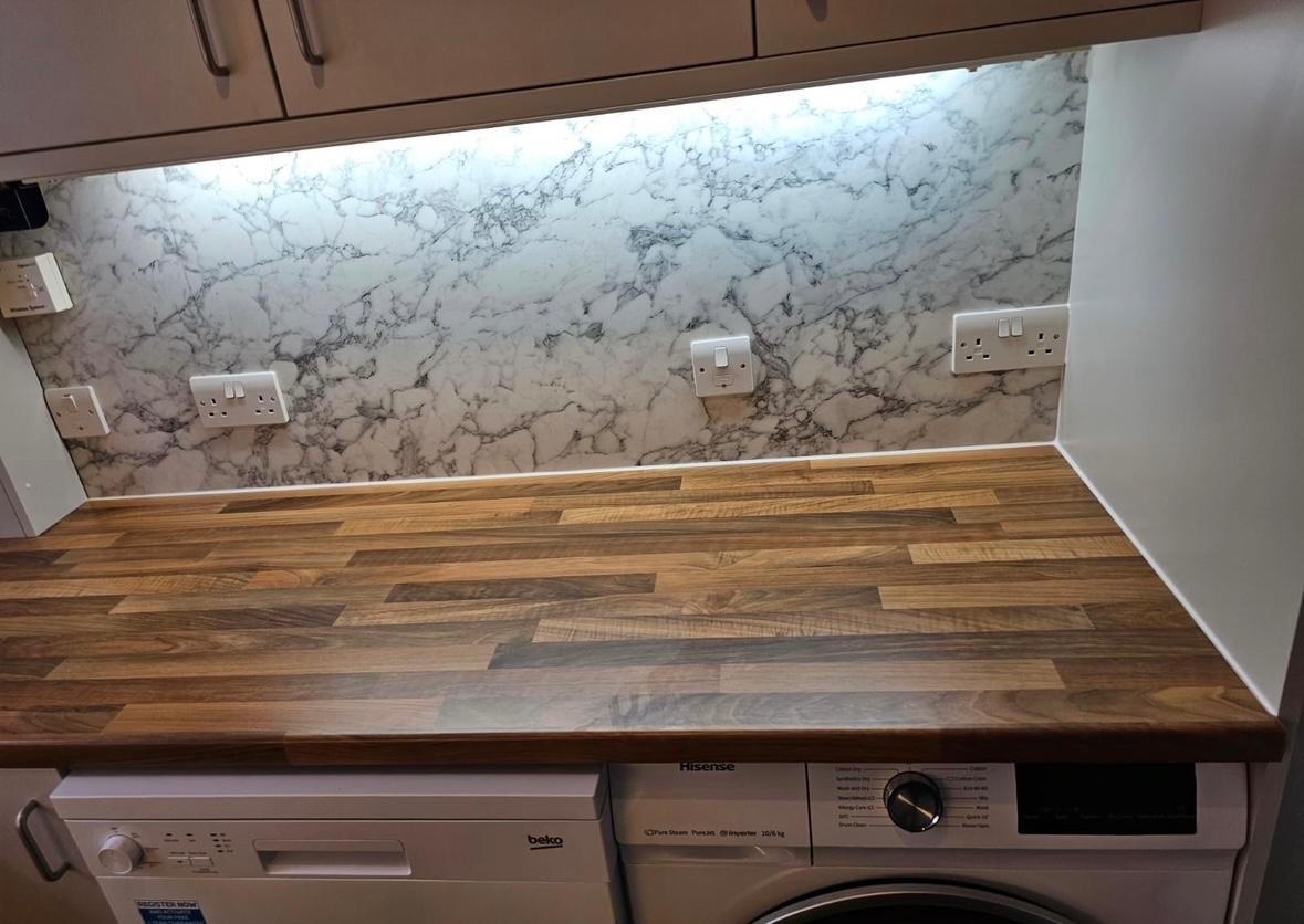 Wood-effect worktop under a lit marble-pattern splashback.