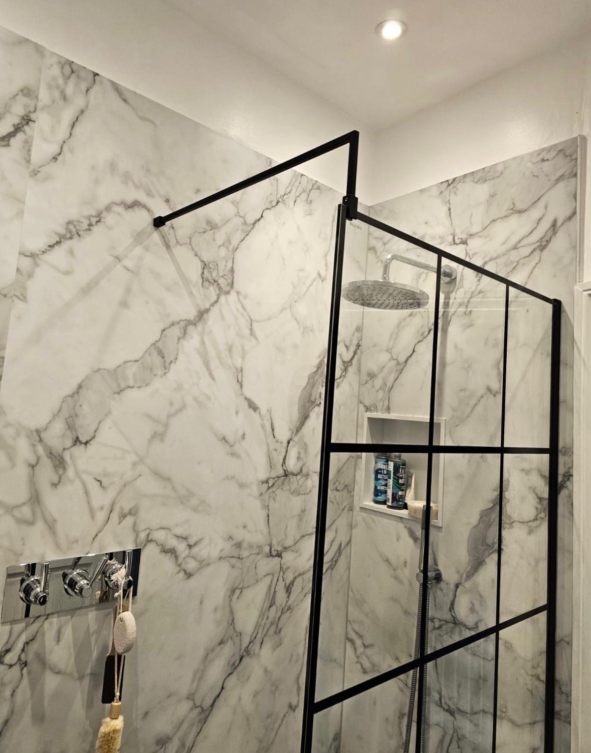 Walk-in shower with a black-framed glass screen and marble-pattern wall.