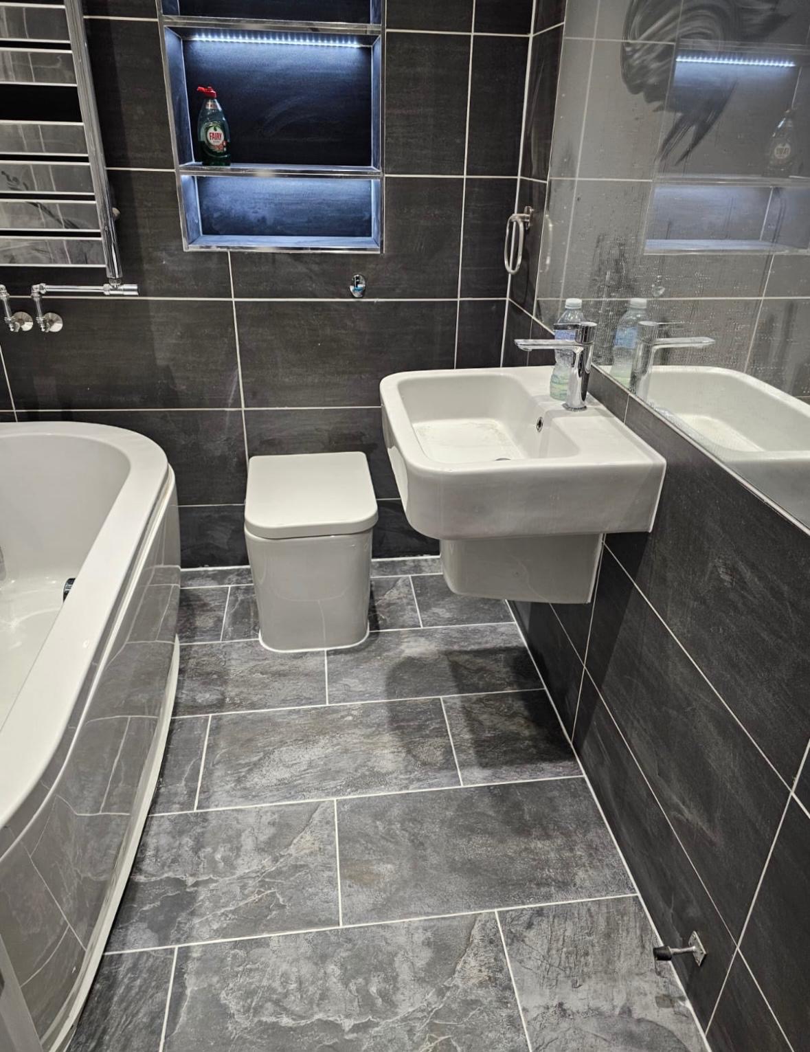 Dark tiled bathroom with a bath, wall-hung basin and toilet.